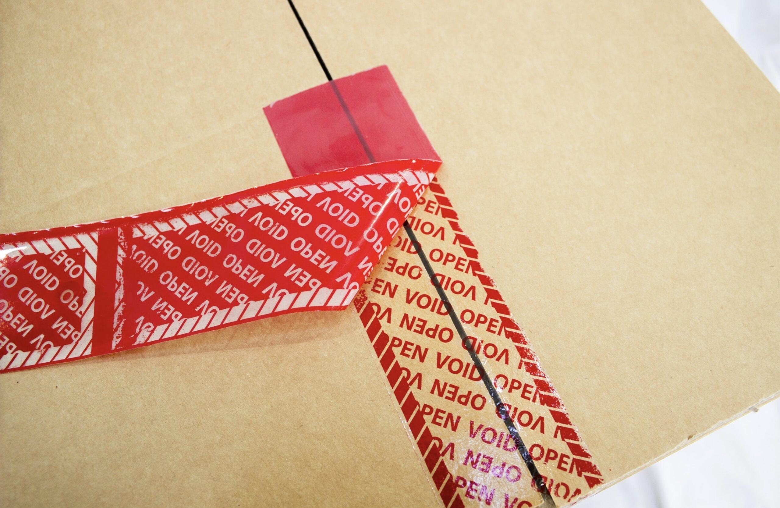 Red tamper-evident security tape applied to a brown cardboard carton